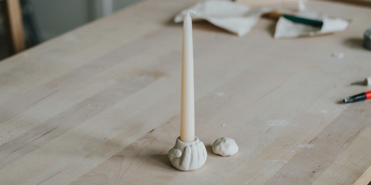 A round white clay taper candle holder with a cream candle in it