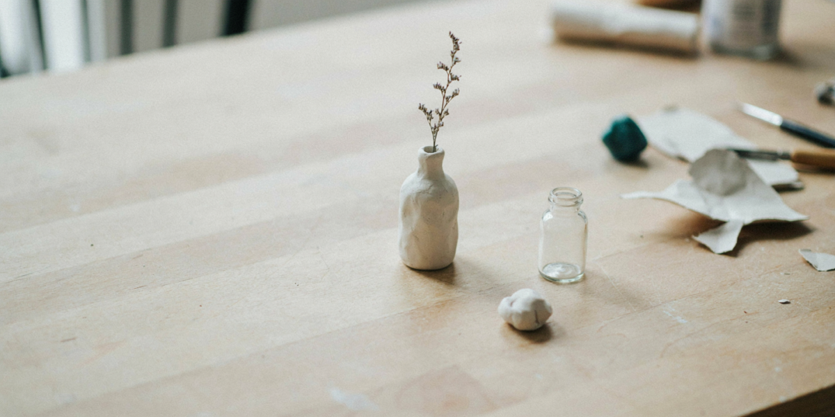 A small clay-covered bud vase holding a single dried stem