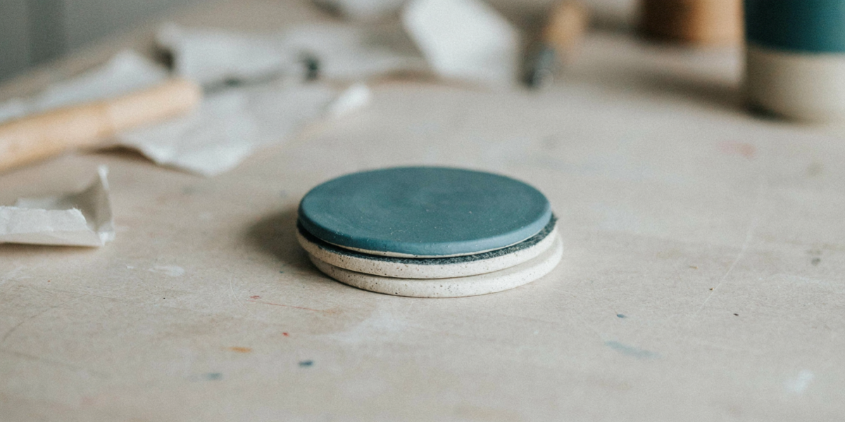 Round painted clay coasters with felt backs stacked beside a mug