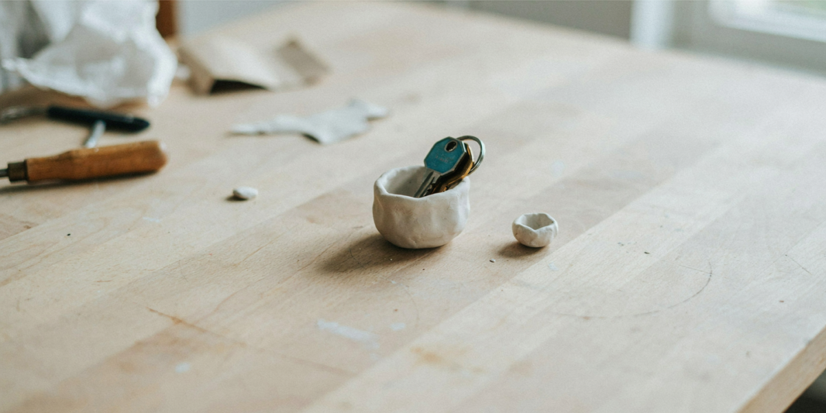 A small white pinch pot holding keys on a pine table