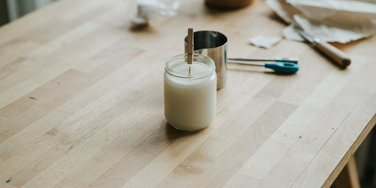 A freshly poured soy candle setting in a jar with the wick held by a clothespin