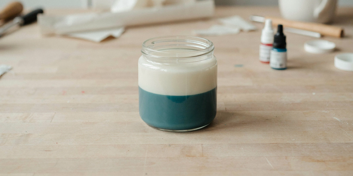 A jar candle with a teal bottom layer and a cream top layer