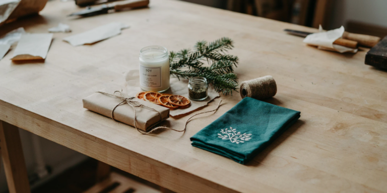 Homemade Christmas gifts on a pine table wrapped in brown paper and twine, a candle, a jar of herb salt and a dried orange garland