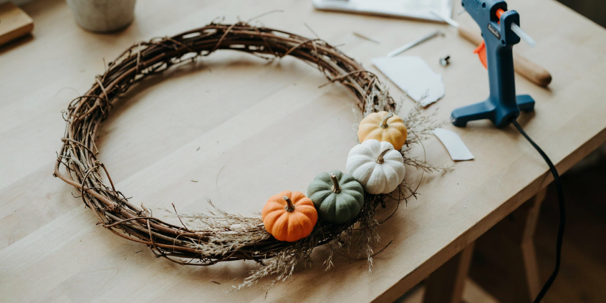 A grapevine wreath with a cluster of small cream and orange faux pumpkins