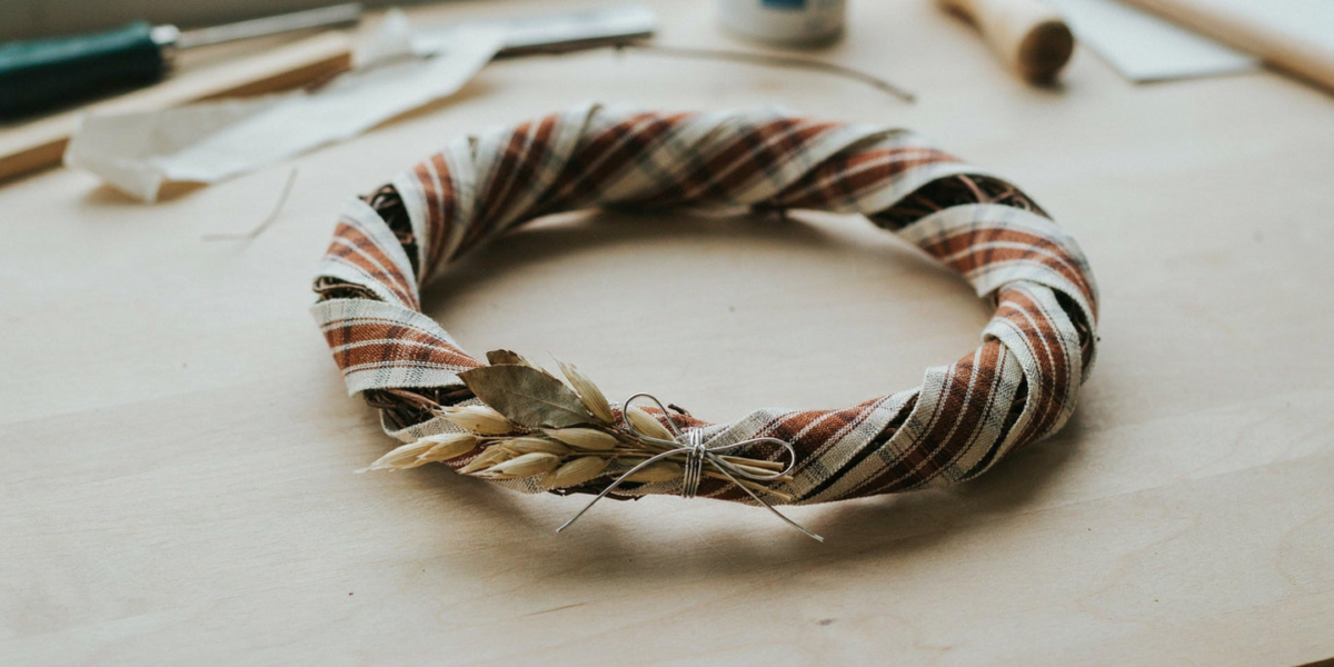 A grapevine wreath spiral-wrapped in plaid ribbon with one bundle of leaves and a bow