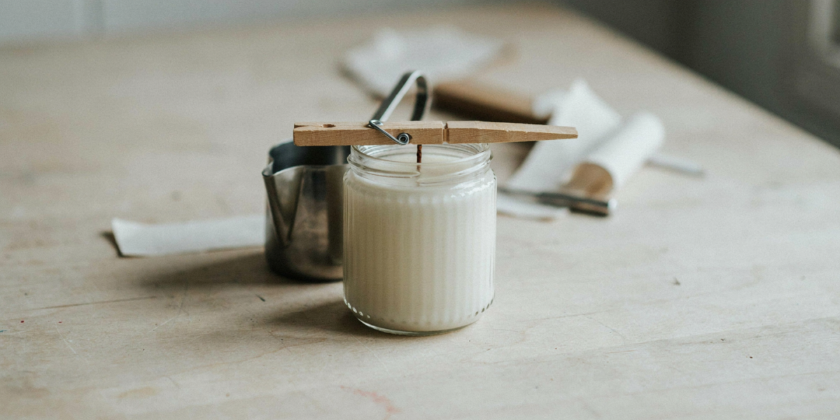 A soy candle setting in a thrifted glass jar with a clothespin holding the wick