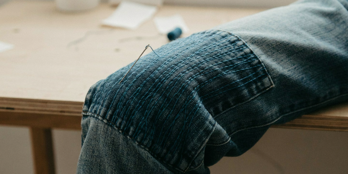 A denim knee patched from behind with rows of teal running stitches