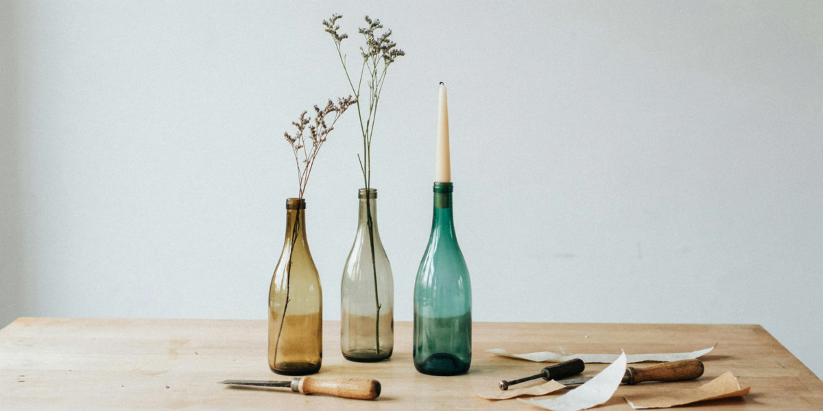 A group of three clear and green wine bottles holding single stems and a taper candle